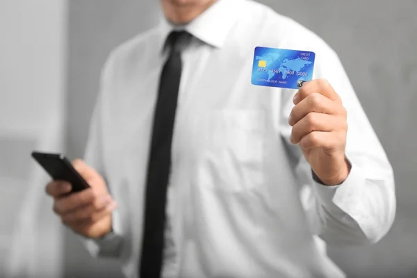 Empresário segurando cartão de crédito e smartphone em fundo embaçado — Fotografia de Stock