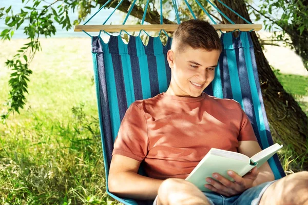 Junger Mann liest Buch, während er sich in der Hängematte im Freien ausruht — Stockfoto