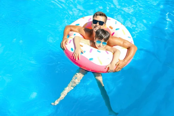 Jovem e seu filho com donut inflável na piscina — Fotografia de Stock