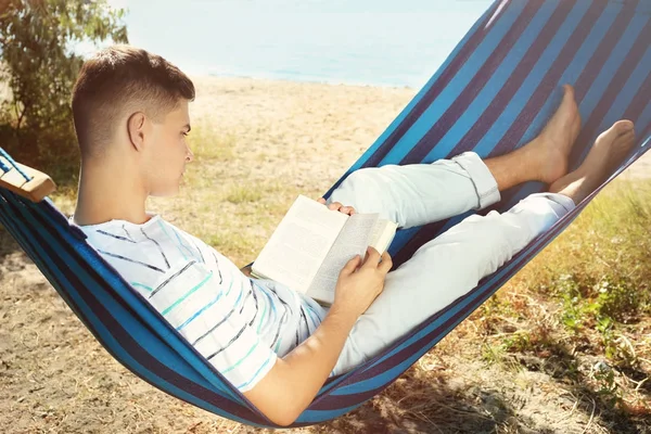 Junger Mann liest Buch, während er sich in der Hängematte im Freien ausruht — Stockfoto