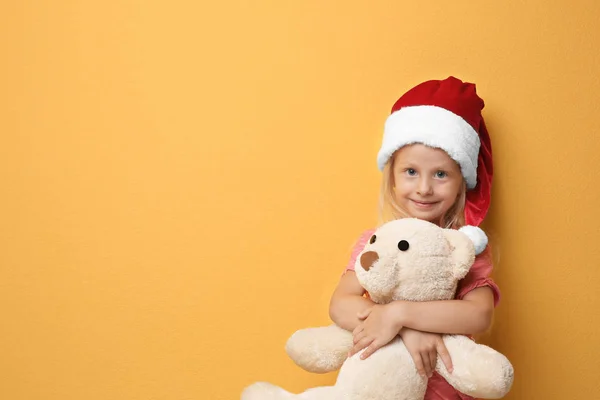 Niedliches Mädchen in Weihnachtsmann-Hut mit Spielzeug auf farbigem Hintergrund — Stockfoto