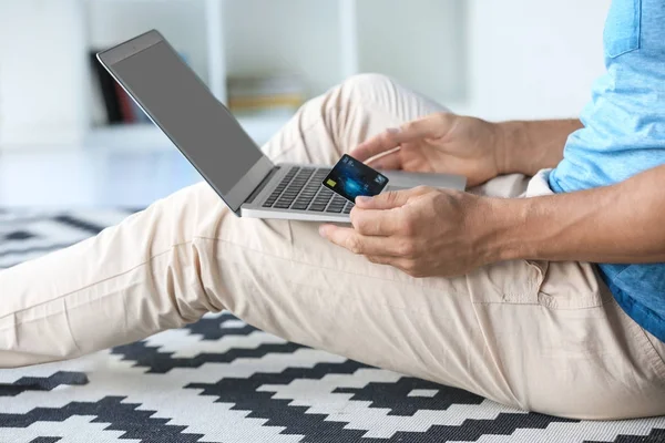 Hombre sosteniendo la tarjeta de crédito mientras usa el ordenador portátil en casa — Foto de Stock