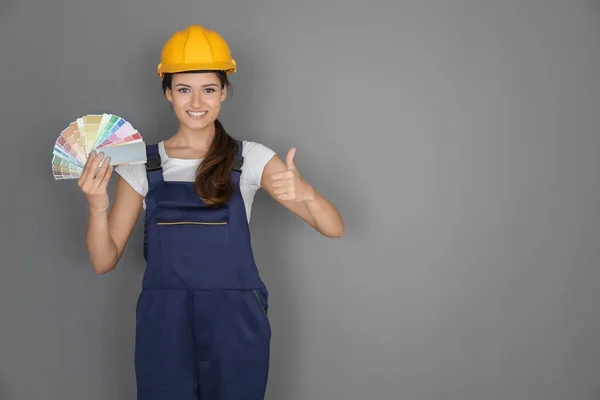 Decoração feminina segurando amostras de paleta de cores contra fundo cinza — Fotografia de Stock