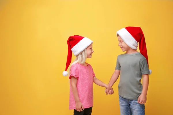 Bambini carini in cappelli Babbo Natale su sfondo di colore — Foto Stock