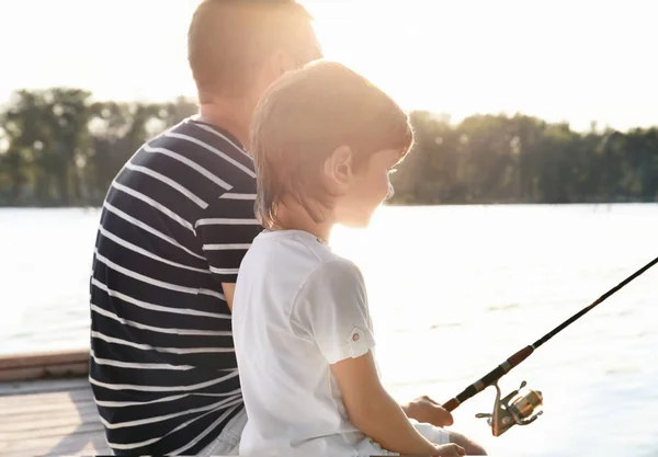 Мальчик с отцом рыбачит с пирса на реке — стоковое фото