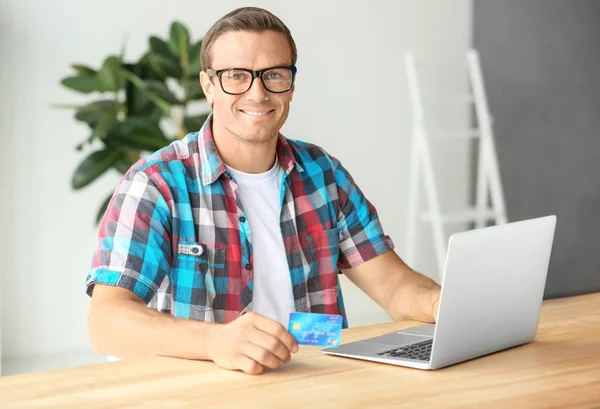 Jovem segurando cartão de crédito ao usar laptop em casa — Fotografia de Stock