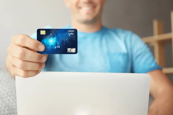 Homem com laptop segurando cartão de crédito dentro de casa — Fotografia de Stock