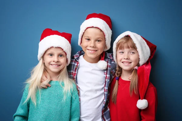 Niedlichen Kindern in Weihnachtsmützen auf farbigem Hintergrund. Weihnachtskonzept — Stockfoto