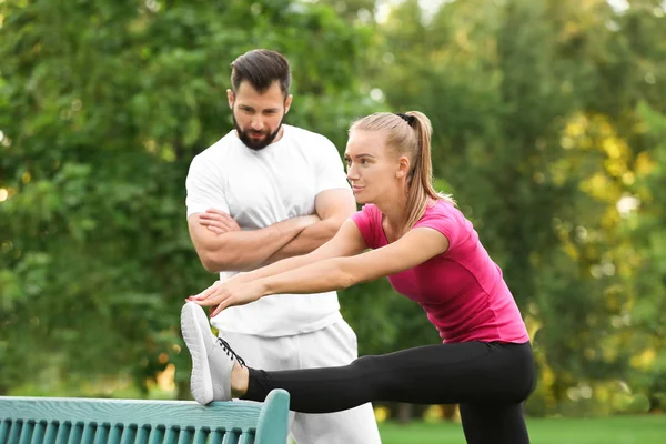 Mladá žena sportovní s trenérem dělat cvičení v parku — Stock fotografie