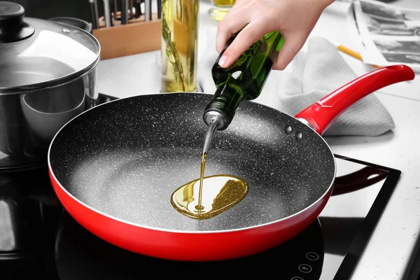 Женщина наливает масло из бутылки в сковородку — стоковое фото