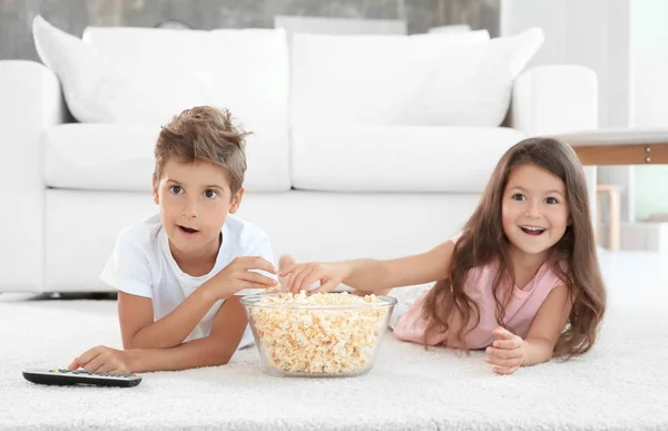 Schattige kinderen eten popcorn tijdens het televisiekijken op verdieping thuis — Stockfoto