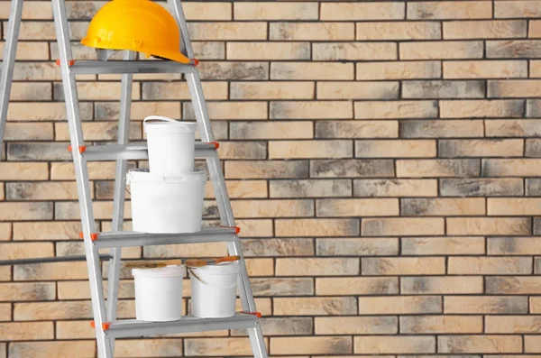 Composition with paint and hard hat on ladder near brick wall — Stock Photo, Image