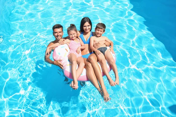 Família feliz com anel inflável relaxante na piscina — Fotografia de Stock