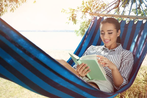 Junge Frau liegt in Hängematte und liest Buch im Freien — Stockfoto