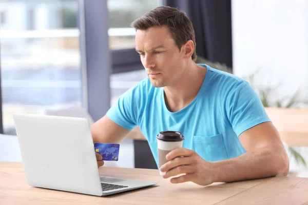 Młody człowiek posiadający karty kredytowej podczas korzystania z laptopa w domu — Zdjęcie stockowe