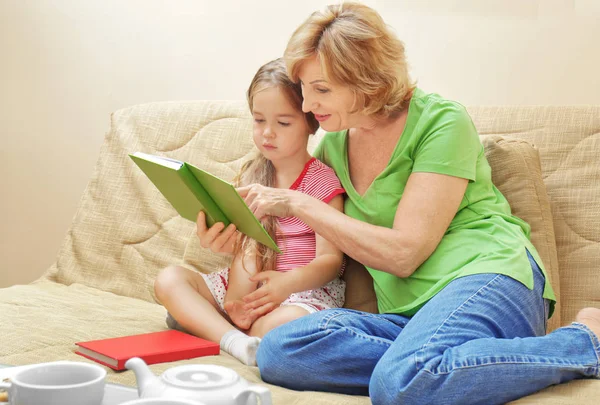 Schattig meisje met oma lezen boek op de Bank thuis — Stockfoto