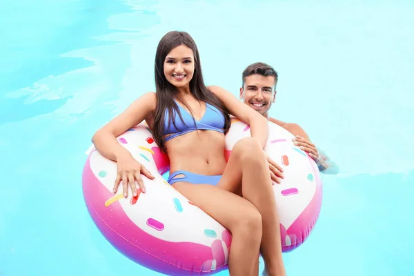 Jovem casal com donut inflável na piscina — Fotografia de Stock