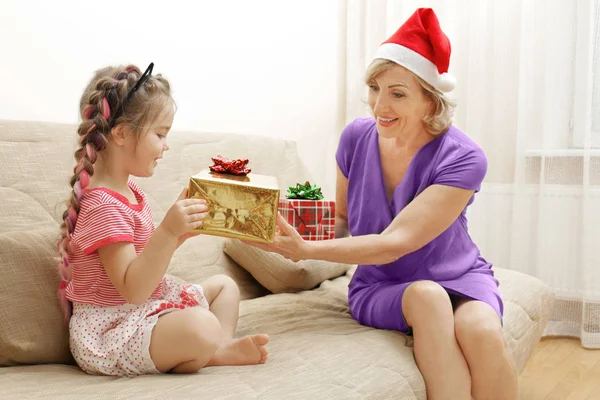 Jolie fille et grand-mère avec des cadeaux de Noël sur le canapé à la maison — Photo