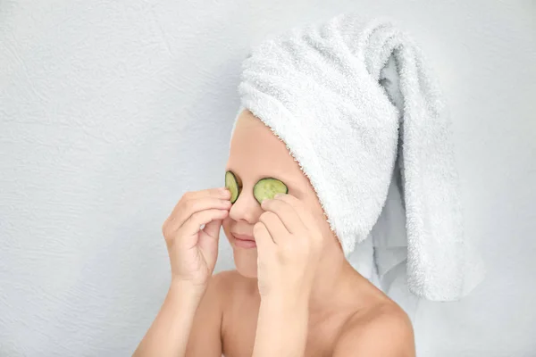 Menina bonito pouco com fatias de pepino nos olhos contra o fundo de luz — Fotografia de Stock