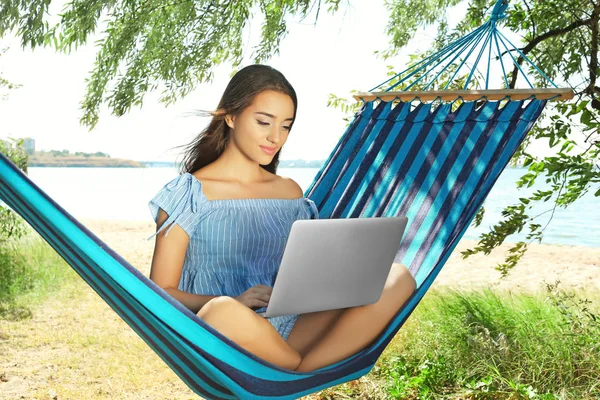 Atractiva mujer con portátil descansando en hamaca al aire libre — Foto de Stock
