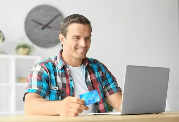 Ung man hålla kreditkort medan du använder laptop hemma — Stockfoto