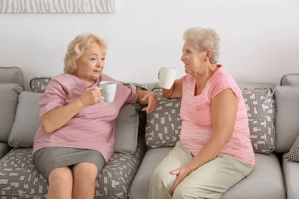 Пожилые женщины пьют кофе, сидя дома на диване — стоковое фото