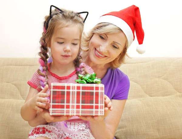 Gadis lucu dan nenek dengan hadiah Natal di sofa di rumah — Stok Foto