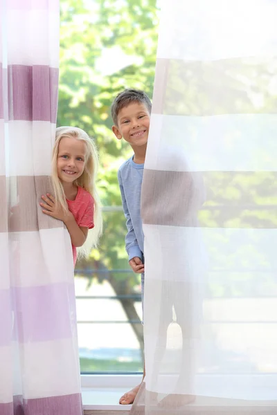 Niedliche kleine Kinder, die sich zu Hause hinter Gardinen verstecken — Stockfoto