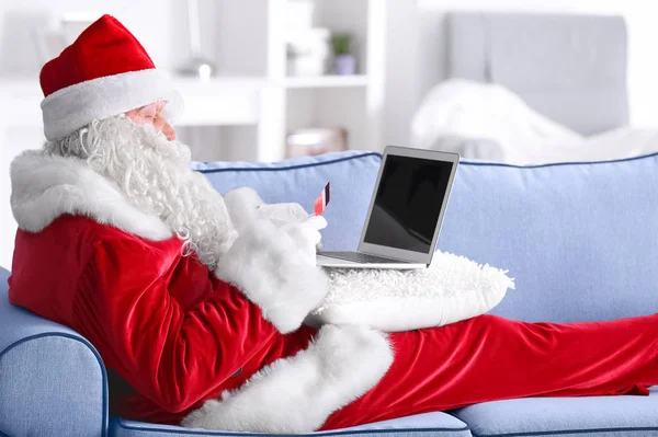 Kerstman met laptop en creditcard op sofa thuis — Stockfoto