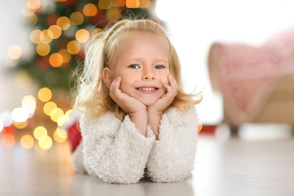 Милая Маленькая Девочка Лежит Полу Дома Против Разряженных Рождественских Огней — стоковое фото