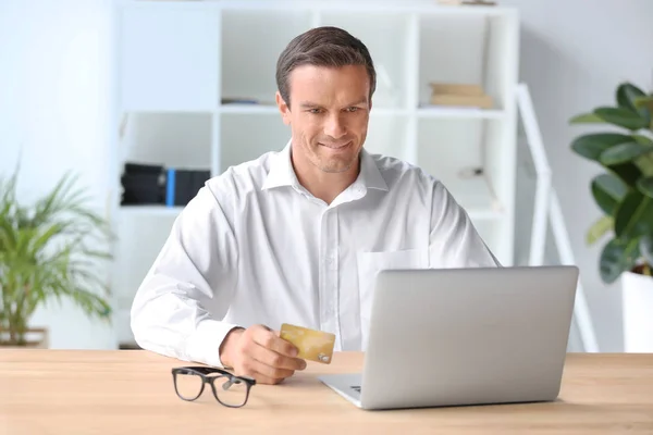 Jeune homme tenant une carte de crédit tout en utilisant un ordinateur portable à la maison — Photo