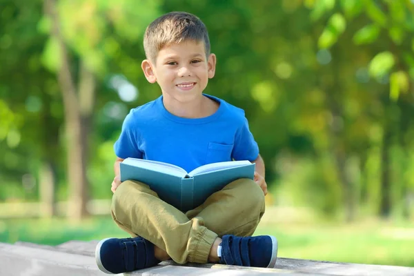 Netter kleiner Junge liest Buch im Park — Stockfoto