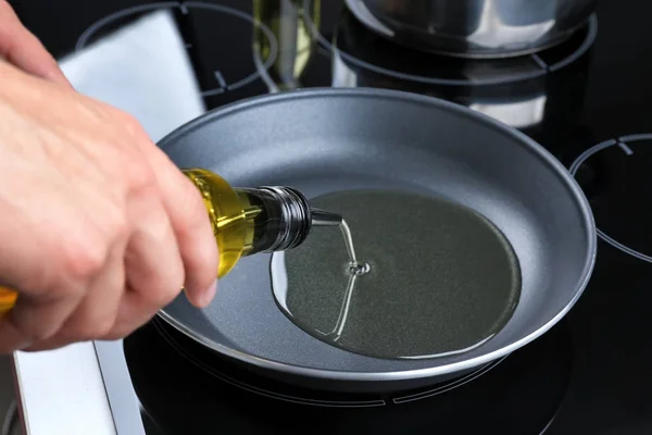 Человек наливает масло из бутылки в сковородку — стоковое фото