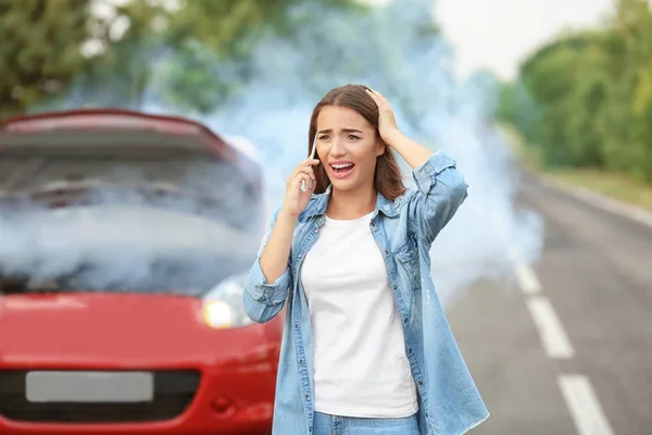 Jovem perturbada com telefone celular perto de carro quebrado — Fotografia de Stock