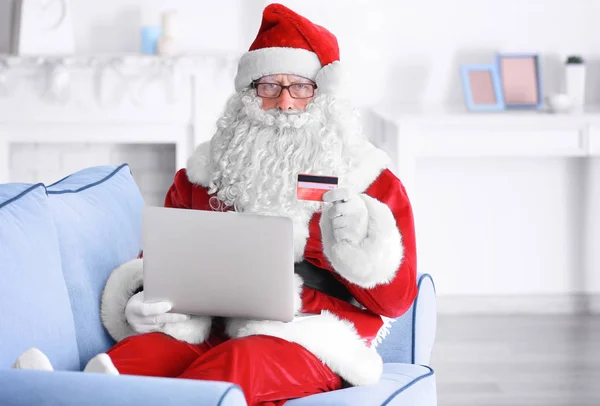 Święty Mikołaj z laptopa i karty kredytowej na kanapie w domu — Zdjęcie stockowe