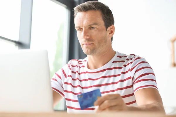 Ung man hålla kreditkort medan du använder laptop hemma — Stockfoto