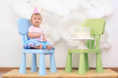 İlk doğum günü partisi için dekore edilmiş oda sandalyede oturan lezzetli pasta ile sevimli küçük kız