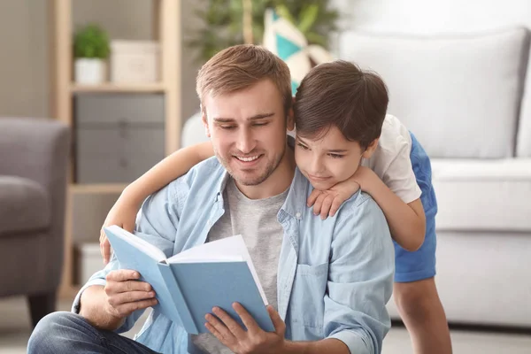 Молодой человек и его маленький сын читают дома книгу — стоковое фото