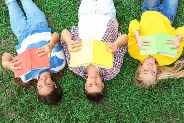 Adolescentes com livros deitados na grama verde — Fotografia de Stock