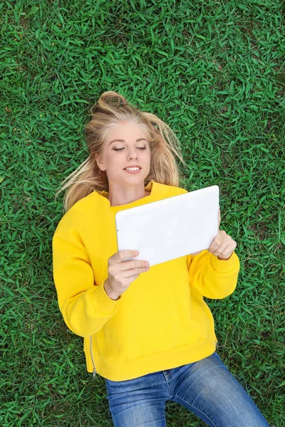 Adolescente chica con la tableta de ordenador acostado en la hierba verde — Foto de Stock