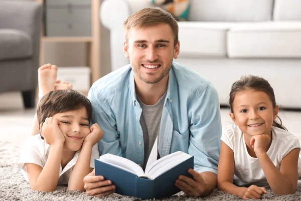 Jonge man en zijn lieve kinderen lezen boek thuis — Stockfoto