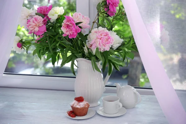 Leckerer Muffin und Vase mit Pfingstrosenblüten — Stockfoto