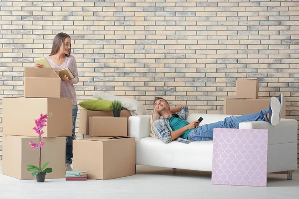 Junge Frau packt Kiste aus, während Mann auf Sofa im neuen Zuhause ruht — Stockfoto