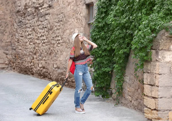 Beautiful young tourist with suitcase on street