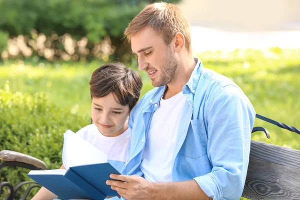 Молодий чоловік і його маленький син читають книгу в парку — стокове фото