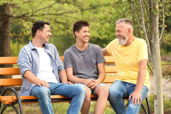 Мальчик-подросток с папой и дедушкой сидит на скамейке в парке — стоковое фото