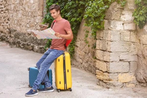 Joven con mapa sentado en la maleta al aire libre — Foto de Stock