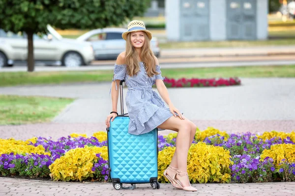 Piękny młody turysta siedzi na walizkę na zewnątrz — Zdjęcie stockowe