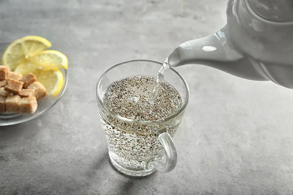 Gieten van water uit theepot in beker met chia zaden — Stockfoto