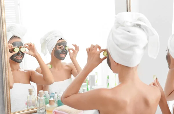 Молоді жінки з масками для обличчя та скибочками огірків у ванній — стокове фото